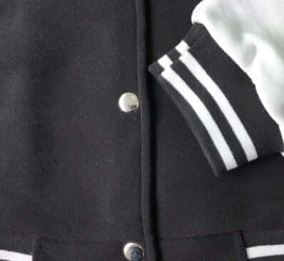 Close-up of a black baseball jacket featuring snap buttons and white ribbed cuffs, highlighting classic varsity style.