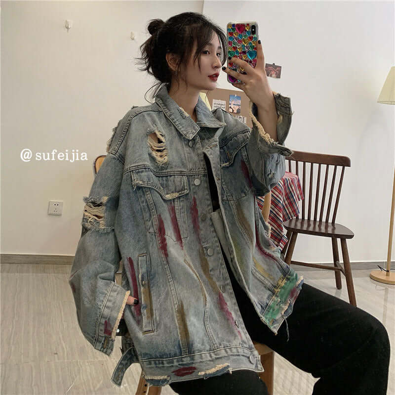 Woman wearing a street hip hop ripped jacket with distressed details and frayed hems, posing in a modern interior.