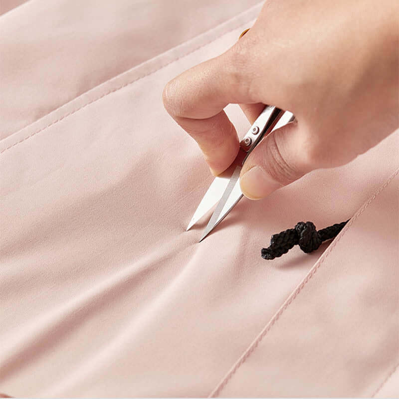 Person using scissors to cut fabric of a waterproof colorblock windbreaker jacket.
